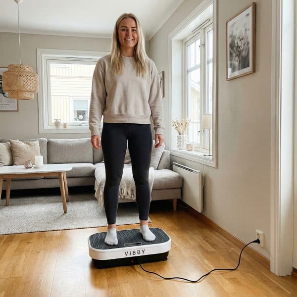 Woman standing relaxed on Vibby vibration plate in a bright, minimal Scandinavian living room